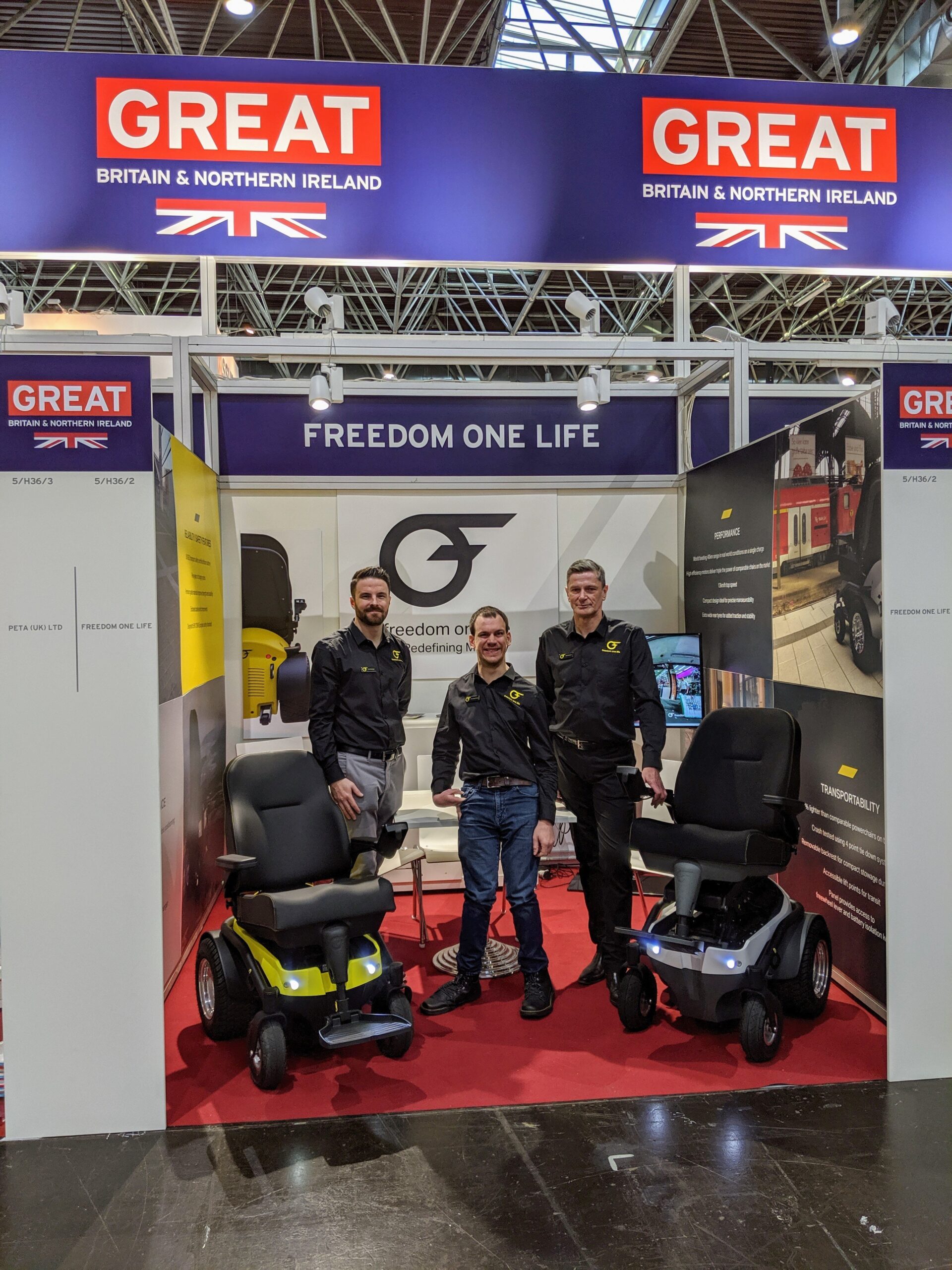 Alex, Scott and Albert standing at the stand at Rehacare with 2 mobility chairs